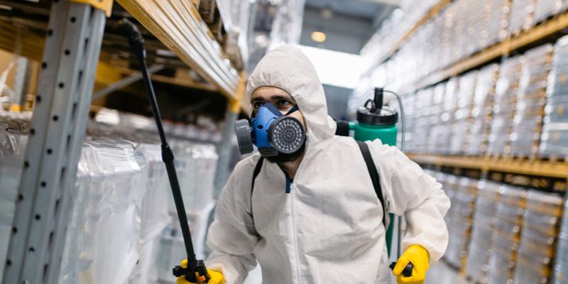 man in protective suit spraying the inside of a warehouse for pests